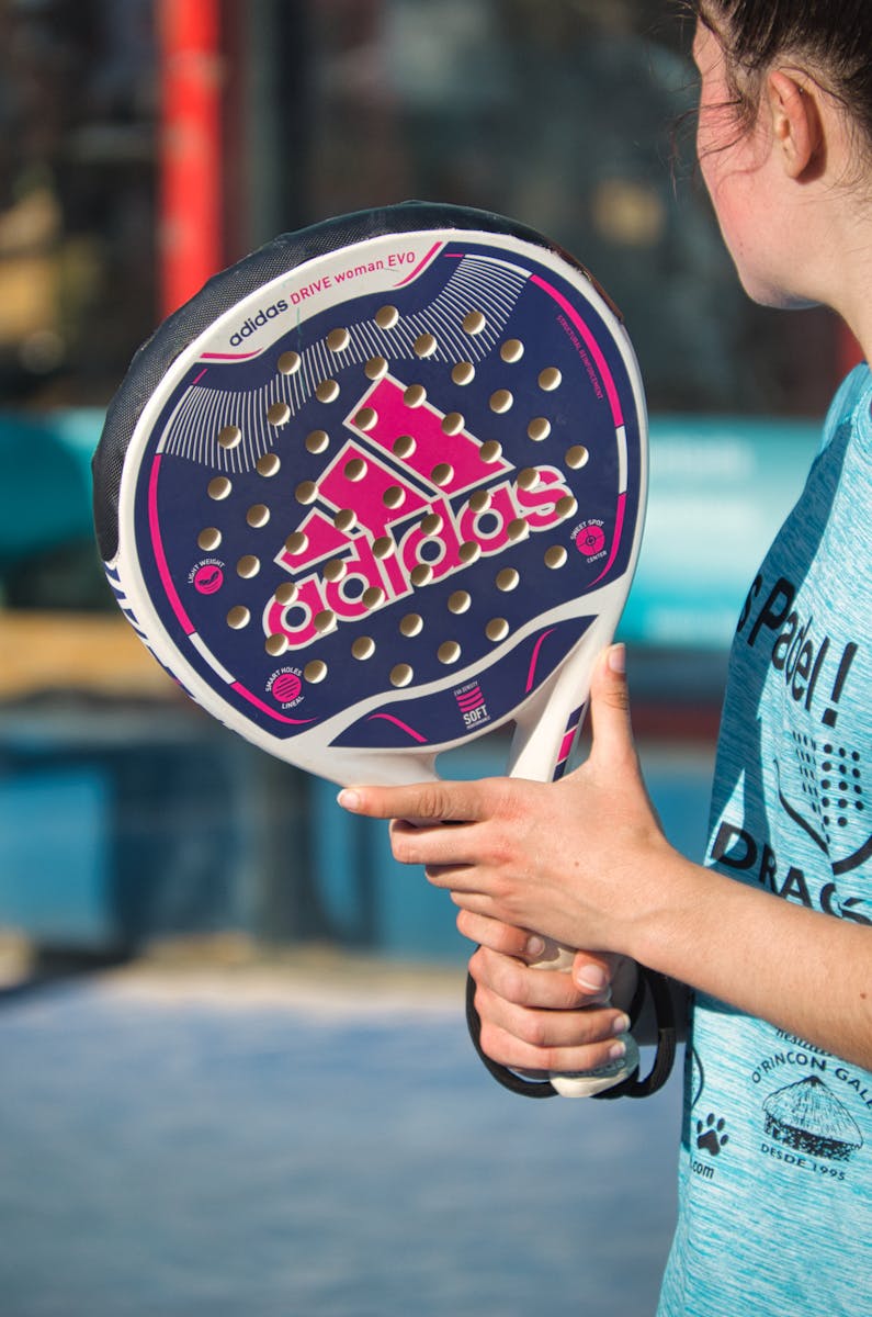Woman playing padel outdoors with Adidas racquet, showcasing sports equipment in action.